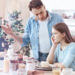Generational misunderstanding. Loving father standing next to a young lady sitting at a table while giving a good talk to her after the daughter did something wrong.