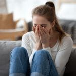 Upset young female sit on couch at home crying over ended relationships, unhappy girl cover face feeling down after breaking up with boyfriend, woman lie on sofa have problems in life