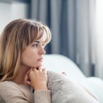Depressed woman sitting on sofa at home, thinking about important things