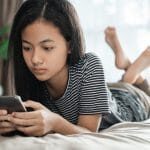 teenager using mobile smart phone at home while laying on the bed